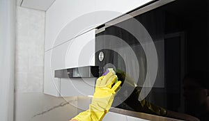 A girl's hand in a yellow glove with a sponge washes the microwave oven from grease and dirt. Foam and anti-grease