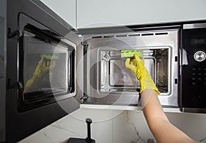 A girl& x27;s hand in a yellow glove with a sponge washes the microwave oven from grease and dirt. Foam and anti-grease