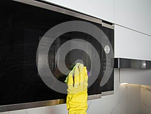 A girl's hand in a yellow glove with a sponge washes the microwave oven from grease and dirt. Foam and anti-grease