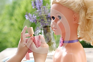 girl's hands applying makeup on doll, playing with set stylist, beautician, hairdresser in garden, on balcony, simulation