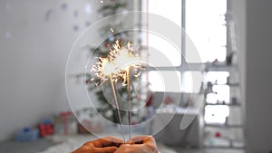Girl`s hands with burning sparkler in front of christmas tree