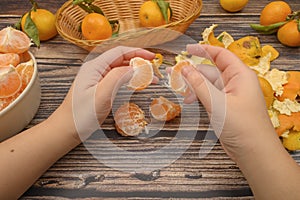 The girl`s hands are cleaning tangerine, tangerines on a twig with green leaves, peeled tangerines in a ceramic dish, tangerine