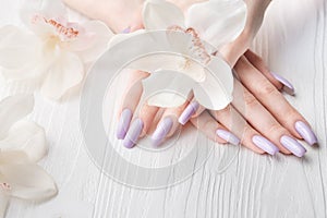 Girl`s hands with delicate purple manicure and orchid flowers