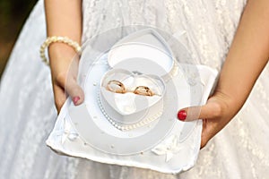 Girl`s hands hold wedding rings in a heart-shaped box