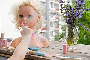 girl's hands imitates painting lips doll, playing with set of stylist, beautician, hairdresser on wooden table in garden, on