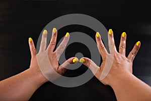 Girl`s hands with manicure. Yellow nails on black background. Spa manicure service