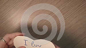 Girl`s hands take a heart shaped note with writing i luv u and takes it from the table.