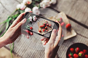 Girl`s hands taking photo of breakfast with strawberries by smartphone. Healthy breakfast