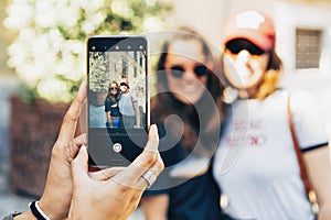 Girl`s hands taking photo with a smartphone of a happy women lesbian couple in Madrid. Same sex relationship and real love concep