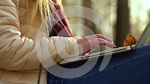Girl`s hands, typing on a laptop keyboard on the street, in the fall.