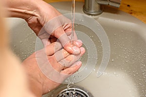 Girl`s hands under running water from the tap in the washbasin