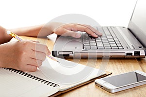 Girl`s hands writing in notebook and using laptop.