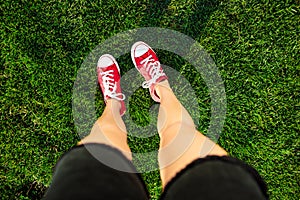 Girl`s legs standing on grass in park. From above.