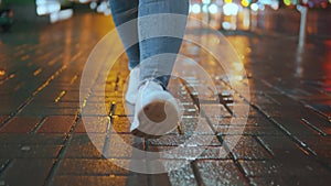 Girl's legs walking in front of the camera on wet paving stones, close-up