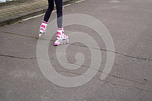 The girl`s legs in white and pink rollers on the asphalt, which is cracked. Riding on a bad road