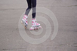 The girl`s legs in white and pink rollers on the asphalt, which is cracked. Riding on a bad road