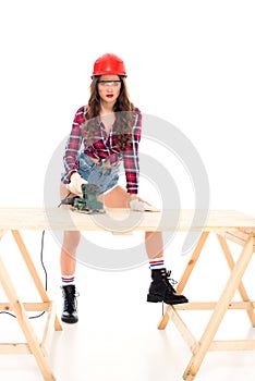 girl in safety helmet working with grind tool at wooden table,