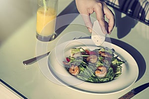 A girl is salting a shrimp salad in a plate. Food Concept