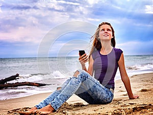 Girl on sand near sea call help by phone.