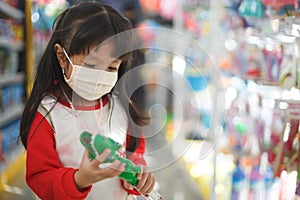 girl in sanitary face mask shopping at toy store. Child wearing protective mask against coronavirus
