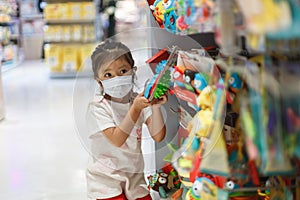 girl in sanitary face mask shopping at toy store. Child wearing protective mask against coronavirus