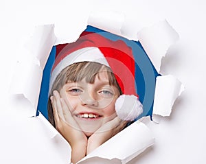 Girl with santa cap looking out of a hole in a paper