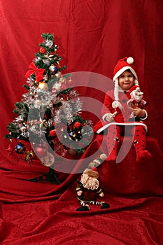 Girl with Santa Claus costume playing with a Christmas tree