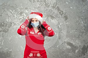 Girl in a Santa Claus hat on a background of a concrete gray wall close-up and copy space. Young woman in a New Year`s costume and