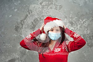 Girl in a Santa Claus hat on a background of a concrete gray wall close-up and copy space. Young woman in a New Year`s costume and