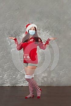 Girl in a Santa Claus hat on a background of a concrete gray wall close-up and copy space. Young woman in a New Year`s costume and