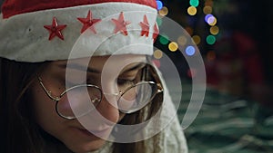 A girl in a Santa Claus hat drinks cocoa from a cup. Christmas Eve