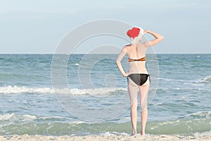 Girl in Santa hat and bathing suit looks into the distance. Sea