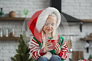 Girl in Santa hat for Christmas eats cookies and cocoa at home in kitchen