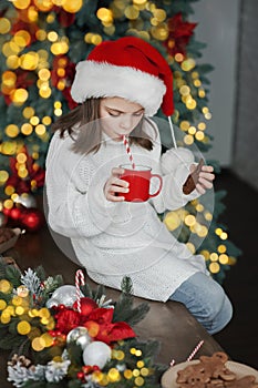 Girl in Santa hat for Christmas eats cookies and cocoa at home in kitchen