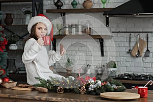 Girl in Santa hat for Christmas eats cookies and cocoa at home in kitchen