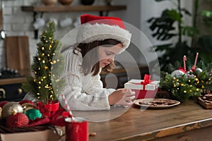 Girl in Santa hat for Christmas eats cookies and cocoa at home in kitchen