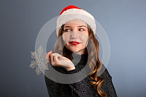 girl in santa hat portrait with big silver snowflake toy posing on gray color background, christmas holiday concept, happy and