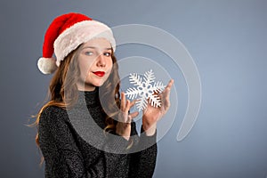 girl in santa hat portrait with big silver snowflake toy posing on gray color background, christmas holiday concept, happy and