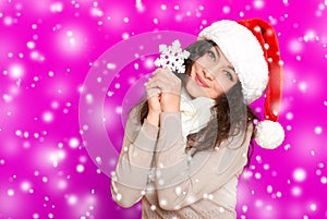 Girl in santa hat portrait with big snowflake toy posing on pink color background, christmas holiday concept, happy and emotions