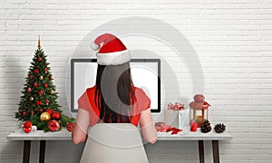Girl with Santa`s hat work on computer at Christmas time
