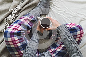 Girl sat on bed in cozy pyjamas drinking a cup of tea