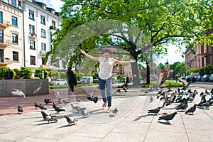 A girl scares a flock of pigeons in the city square