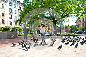 A girl scares a flock of pigeons in the city square