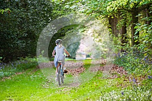 Girl in school uniform and cycle helmet riding bike along a tree lined country track