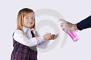 A girl in a school uniform looks at the camera smiling disinfects hands with antiseptics before entering school