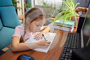 Girl schoolgirl does school homework at home in front of a computer photo