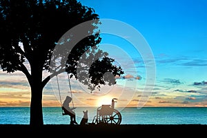 Girl schoolgirl invalid sitting on a swing under a tree by the sea, reading a book, beside a wheelchair and her dog