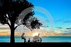 Girl schoolgirl invalid sitting on a swing under a tree by the sea, reading a book, beside a wheelchair and her dog photo