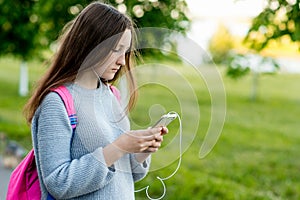 Girl schoolgirl student. In the summer on the street. In his hands holds a smartphone. Play music reads and writes