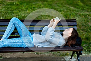 Girl schoolgirl. In summer, he lies on a bench in city. In the hands of holding a smartphone, watching a video. Concept